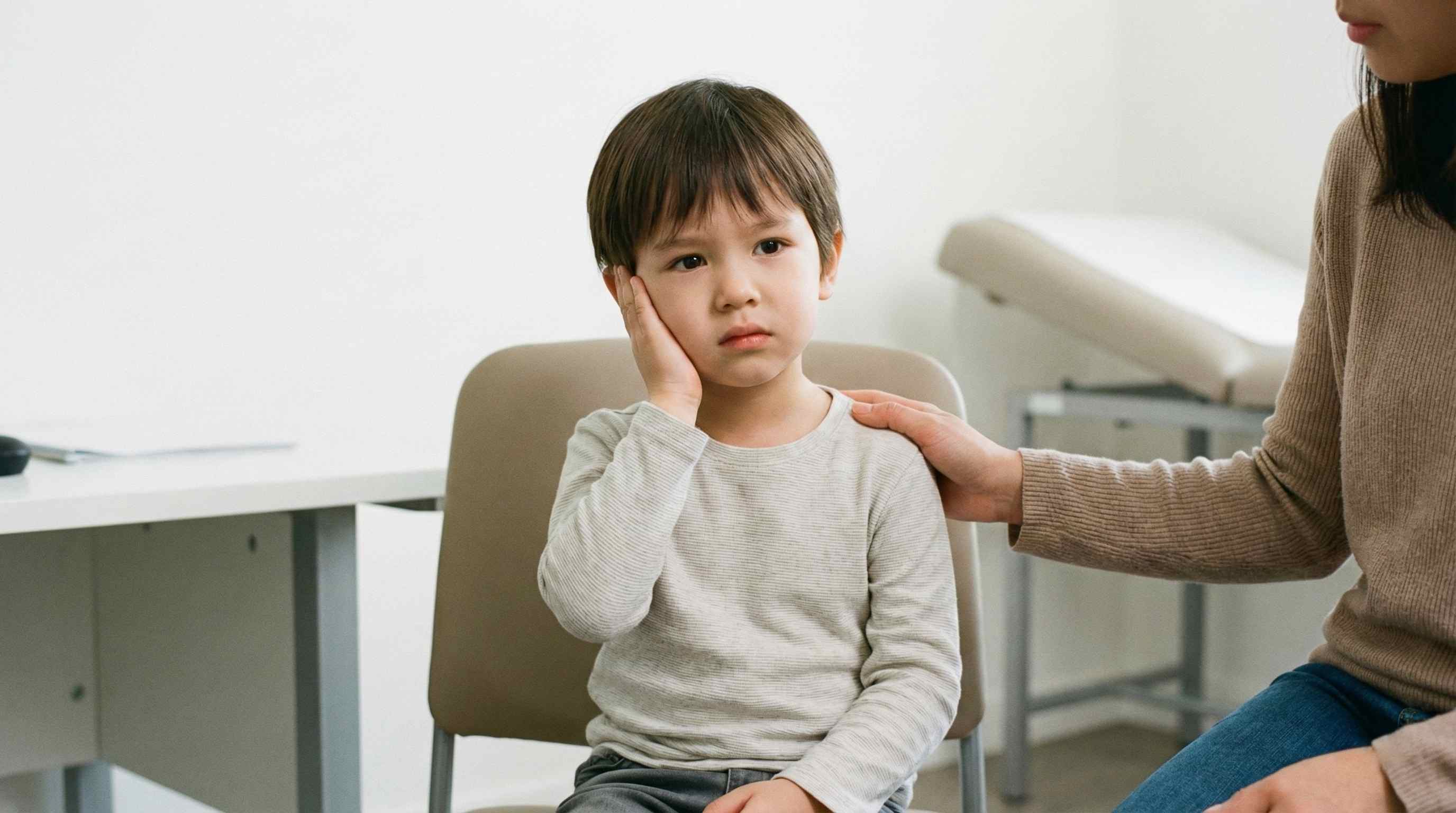 Barn i undersøgelsesrum holder hånd mod øret med øreubehag, mens en forælder sidder ved siden af